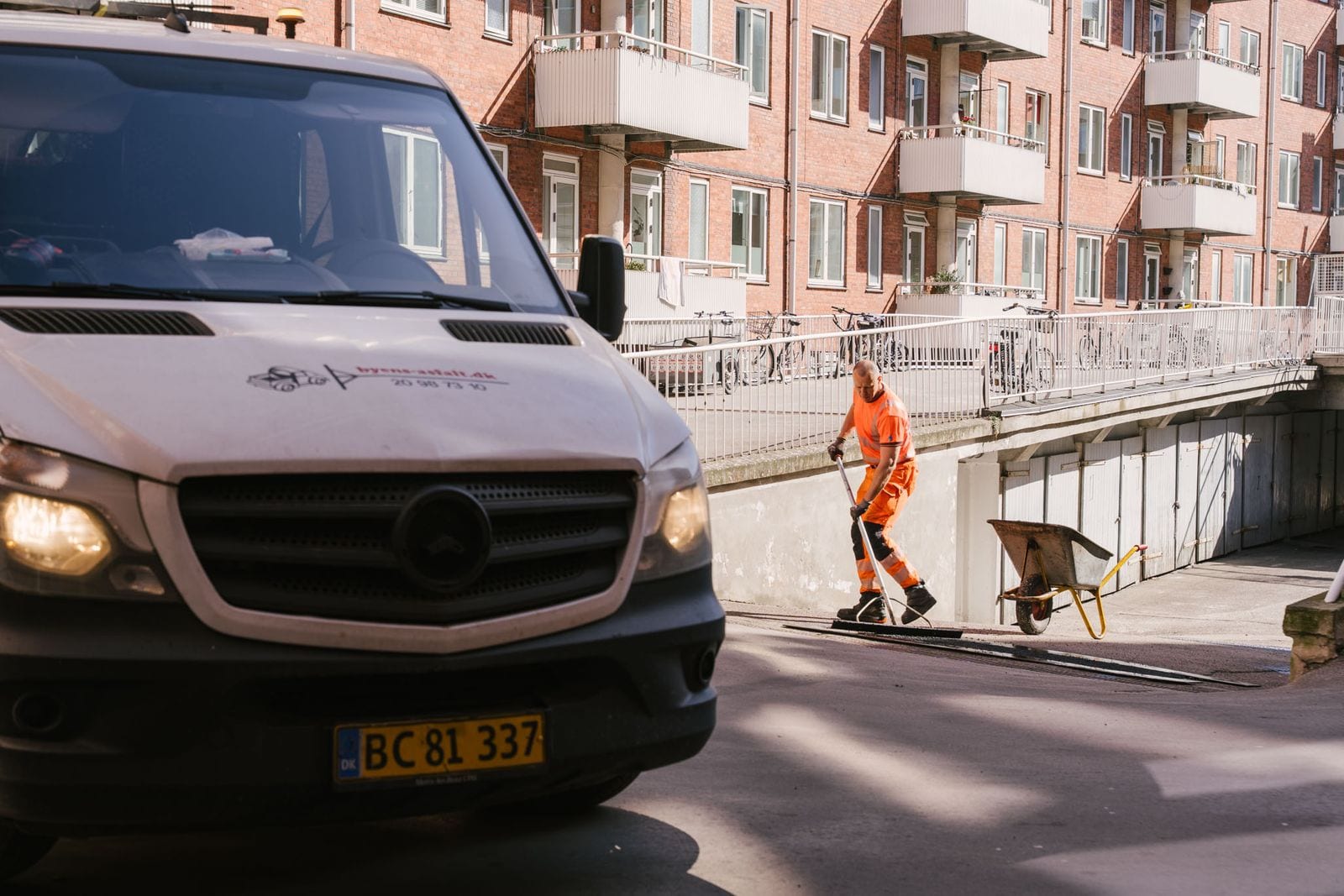 Byens Asfalts varebil ved en opgave, mens en medarbejder arbejder i baggrunden